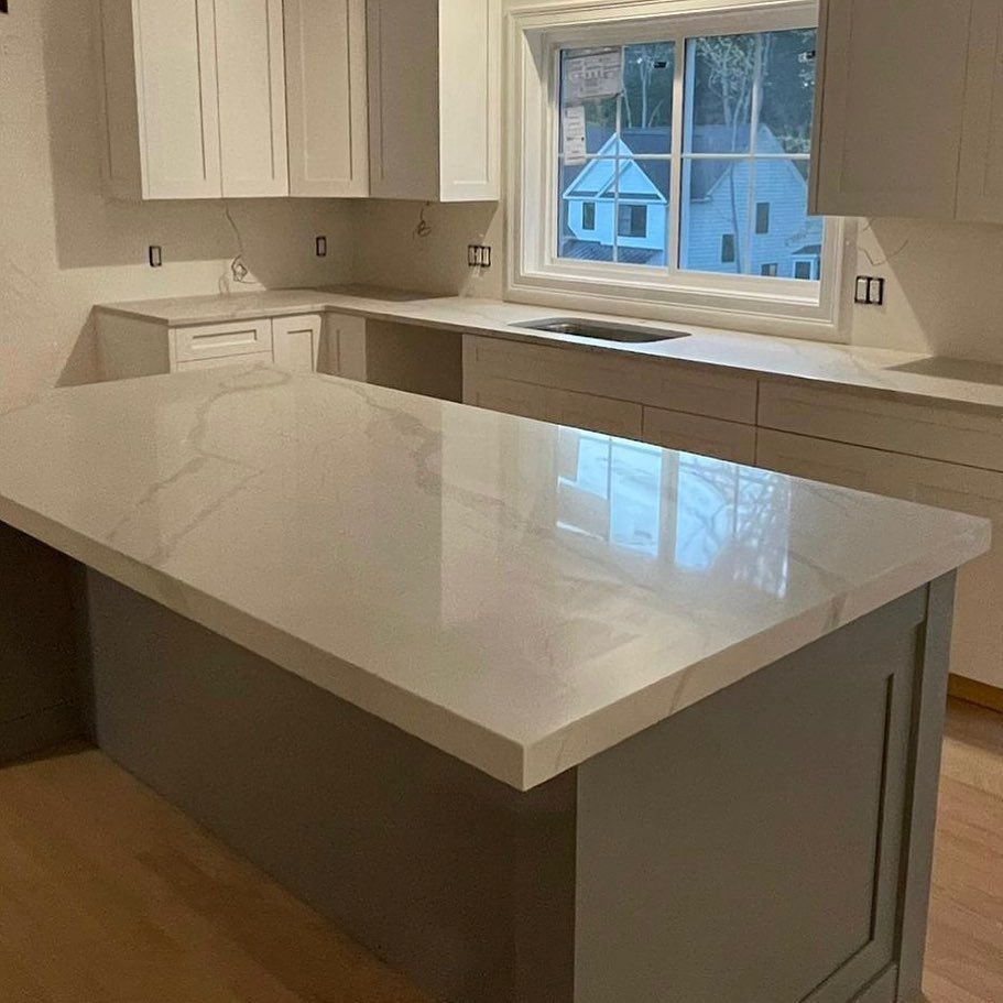 A kitchen with white cabinets , a large island , a sink , and a window.