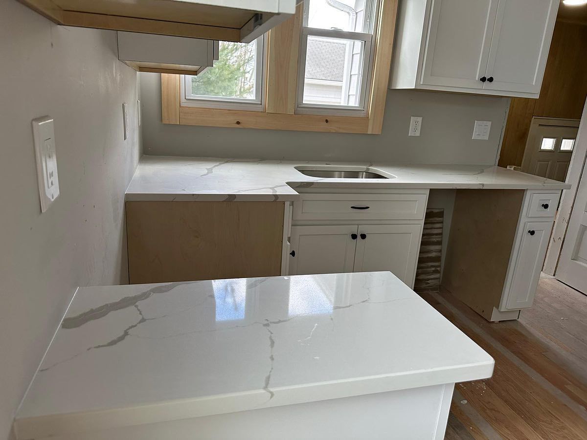 A kitchen with white cabinets , white counter tops , a sink and a window.