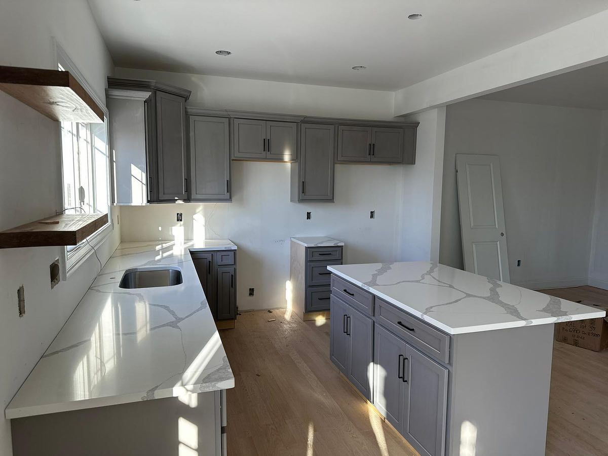 A kitchen with gray cabinets , white counter tops , and a large island.