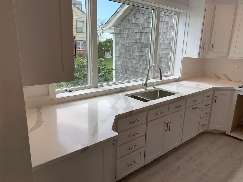 A kitchen with white cabinets , a sink , and a window.