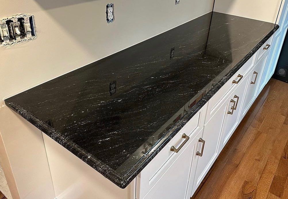 A kitchen with a black granite counter top and white cabinets.