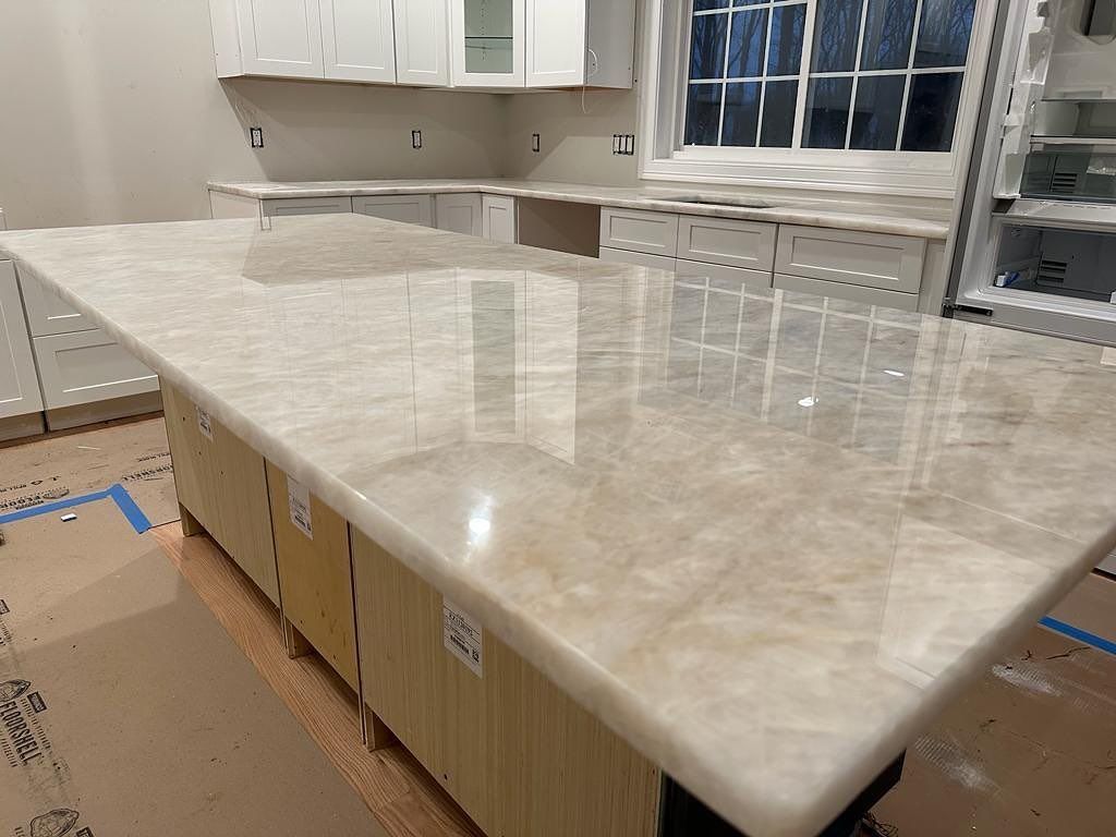 A kitchen with a large marble counter top and white cabinets.