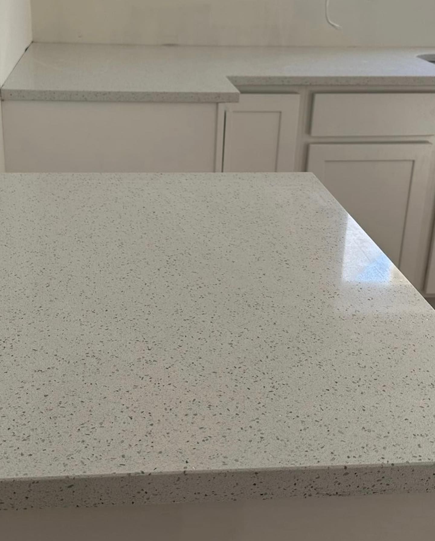 A white counter top in a kitchen with white cabinets and a sink.