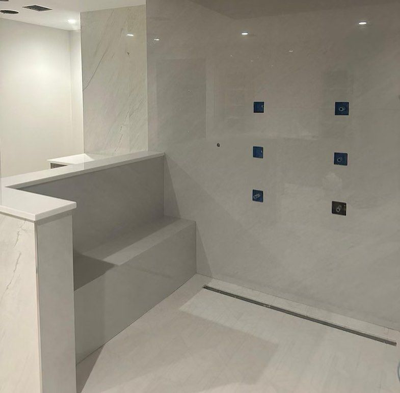 A bathroom with a bench and a shower with blue tiles on the wall.
