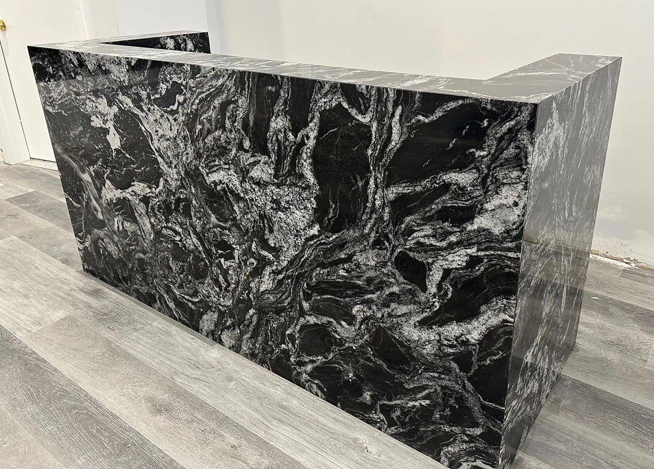 A black and white marble counter top is sitting on a wooden floor.