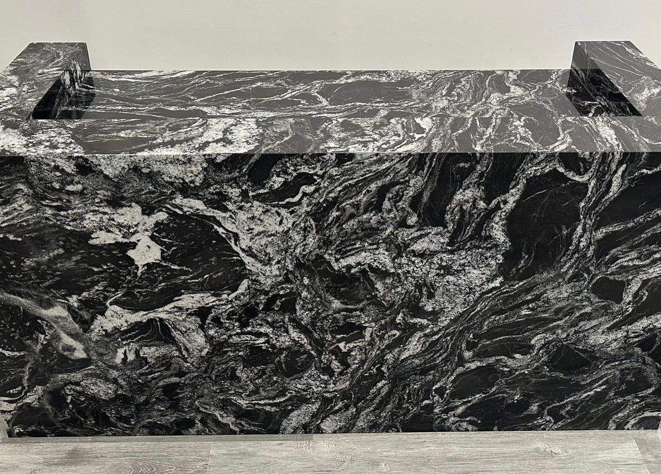 A black and white photo of a marble counter top with a sink.