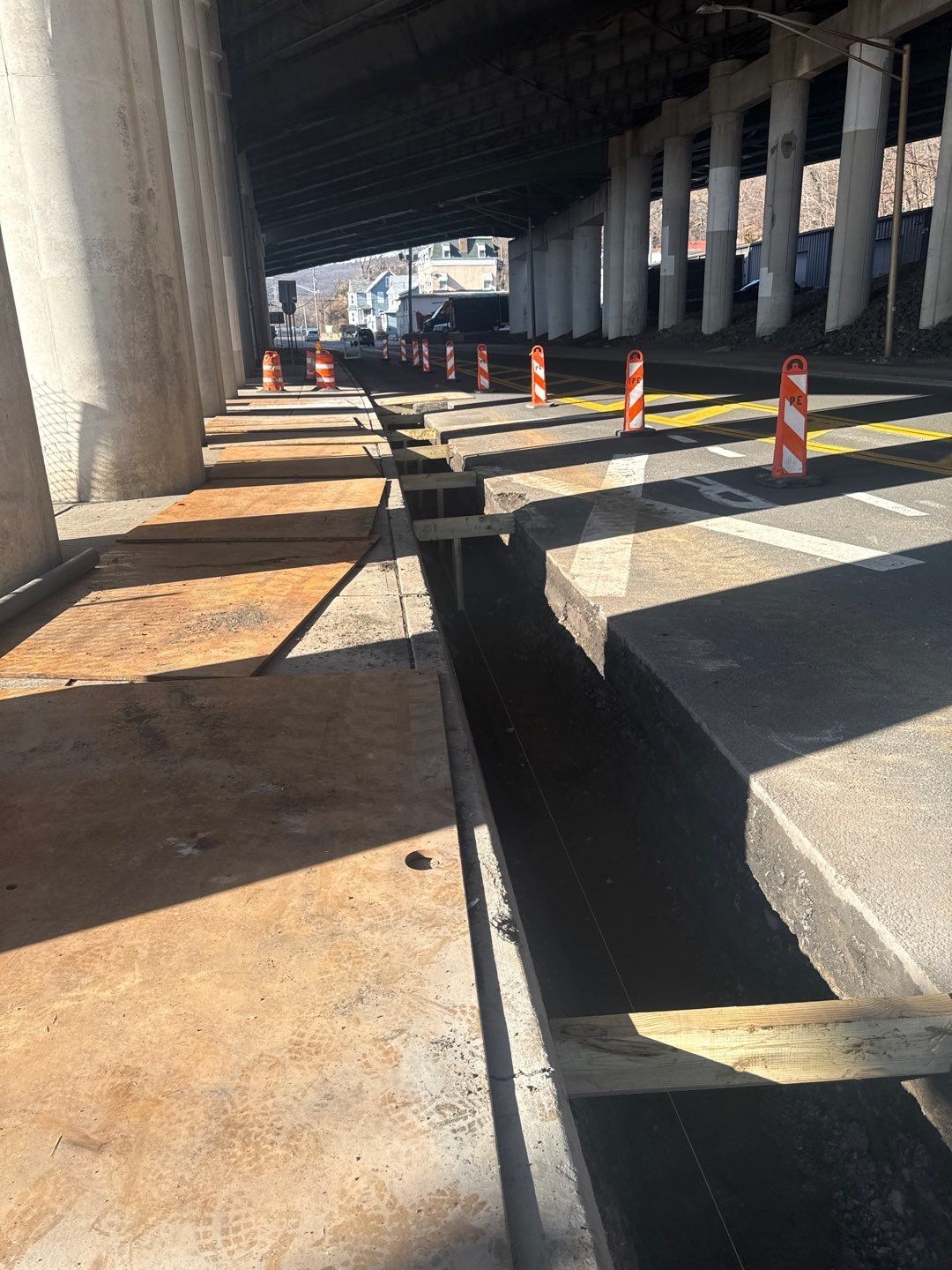 Construction under a bridge. Roadway with orange traffic cones and exposed concrete.