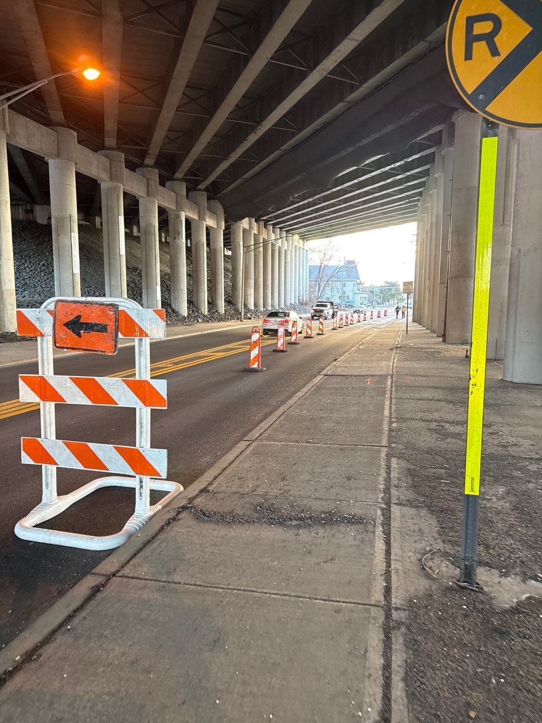 Road under bridge with construction barriers and a R turn sign.