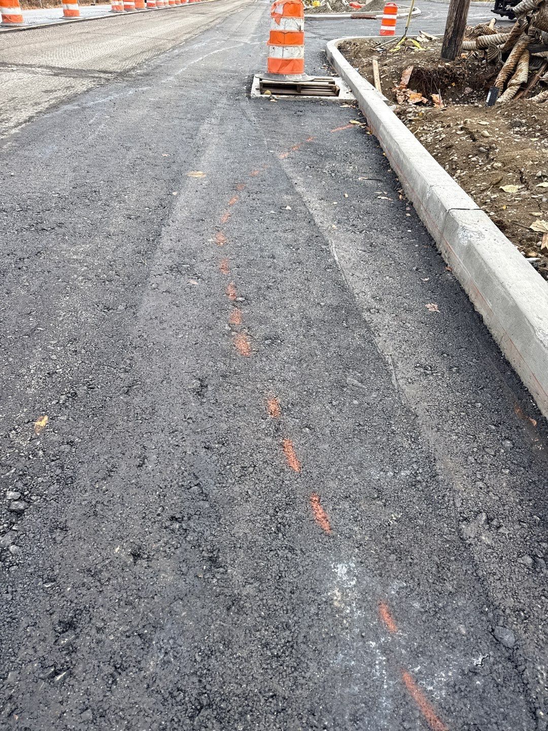 Newly paved road with orange construction cones and concrete curb.