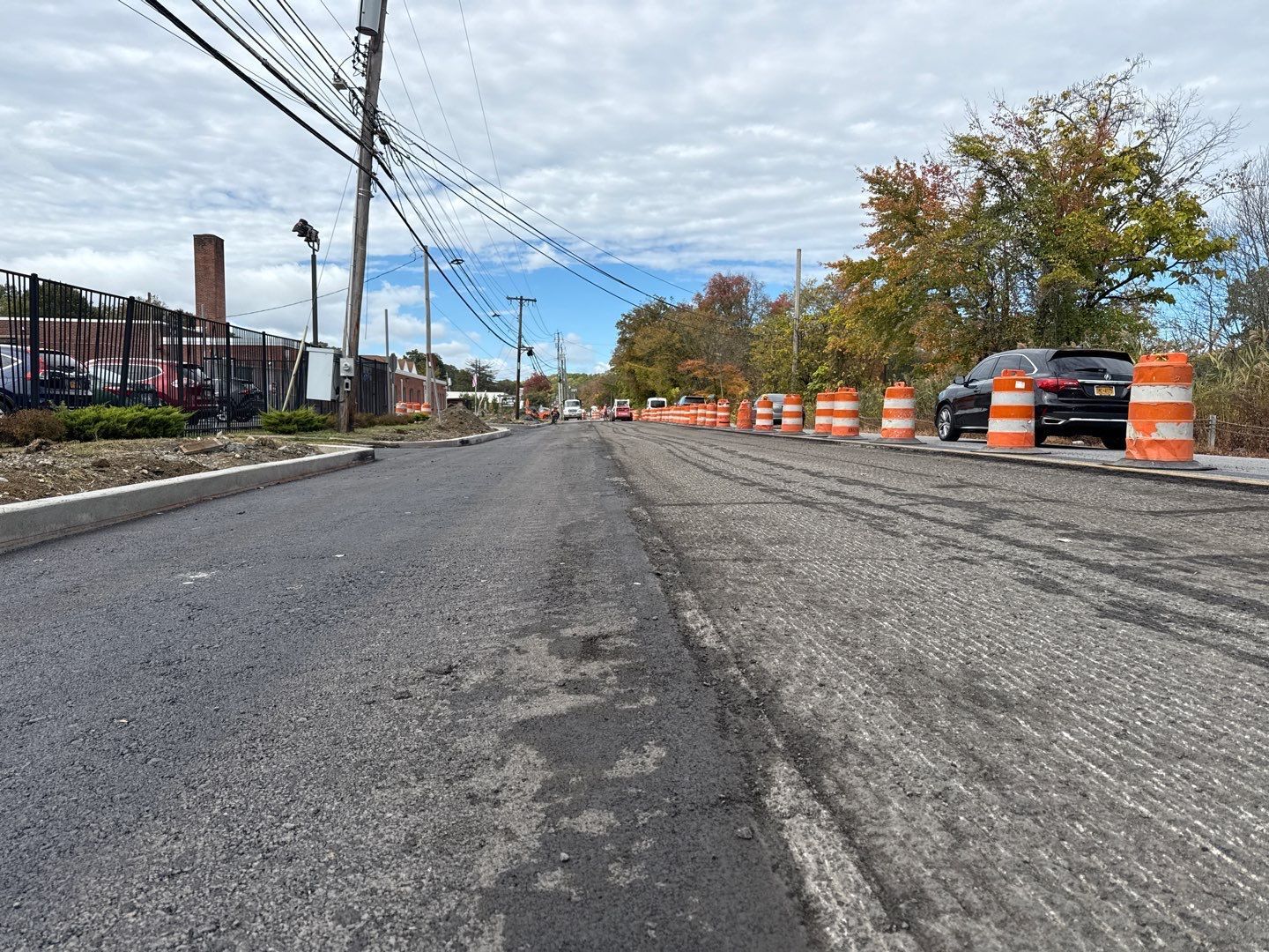 Road under construction with orange traffic barriers, overhead power lines, and a cloudy sky.