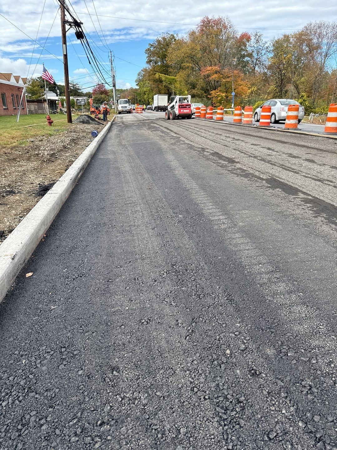 Freshly paved road under construction, lined with orange traffic cones.