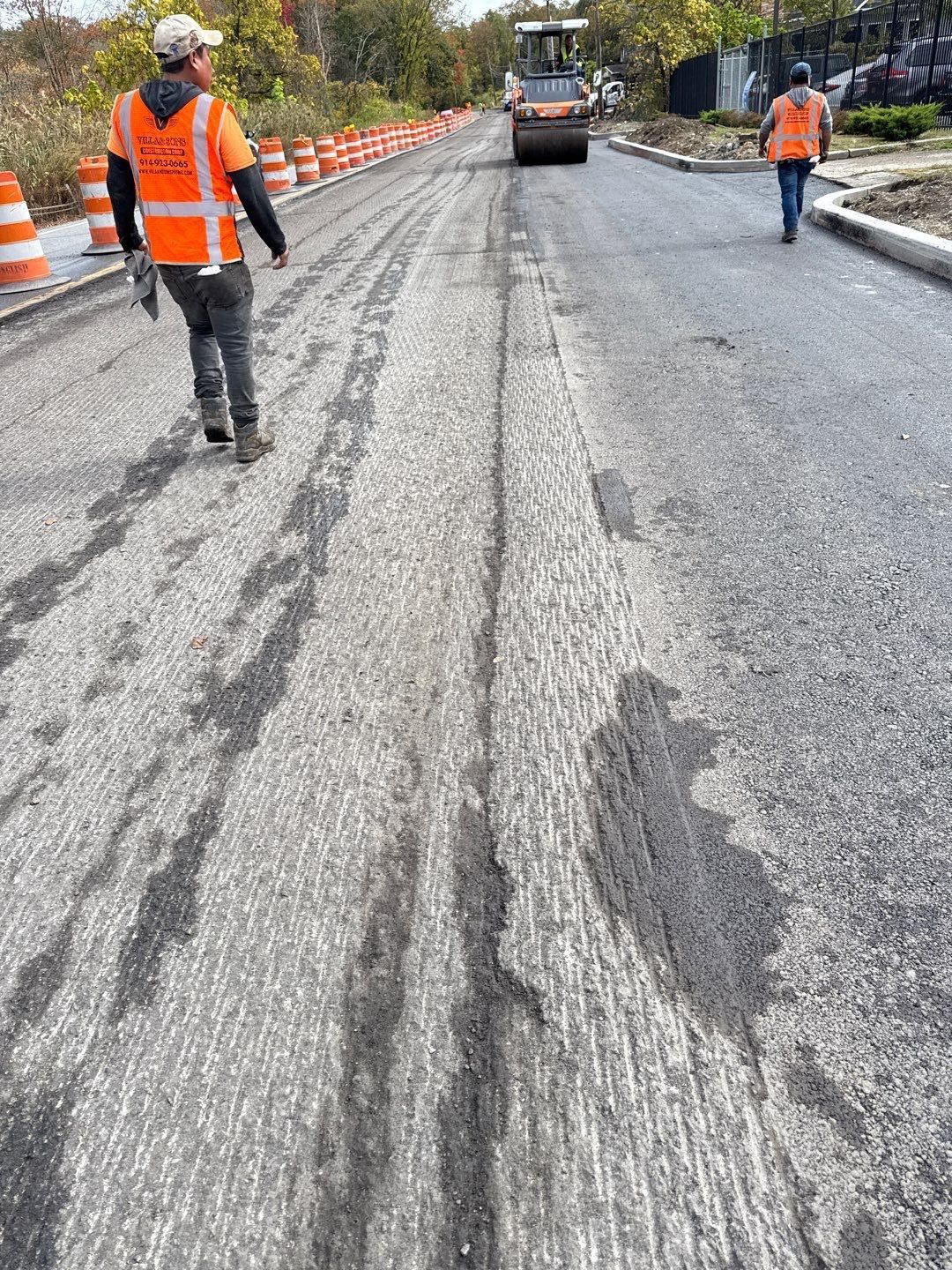 Road construction with workers in orange vests; asphalt being paved with a steamroller.
