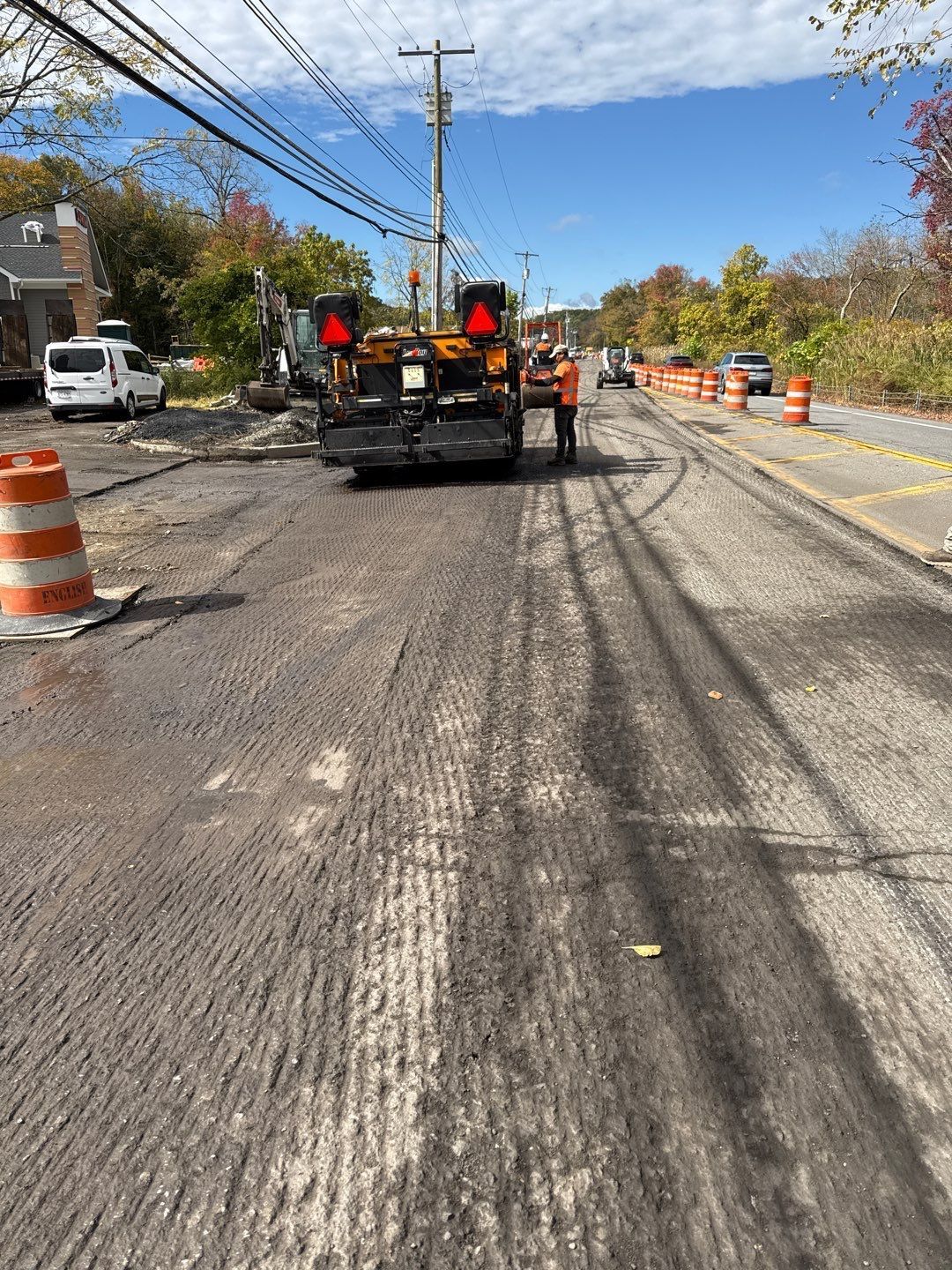 Road construction: Truck with lights on stripped asphalt road, cones, worker, trees and sky.