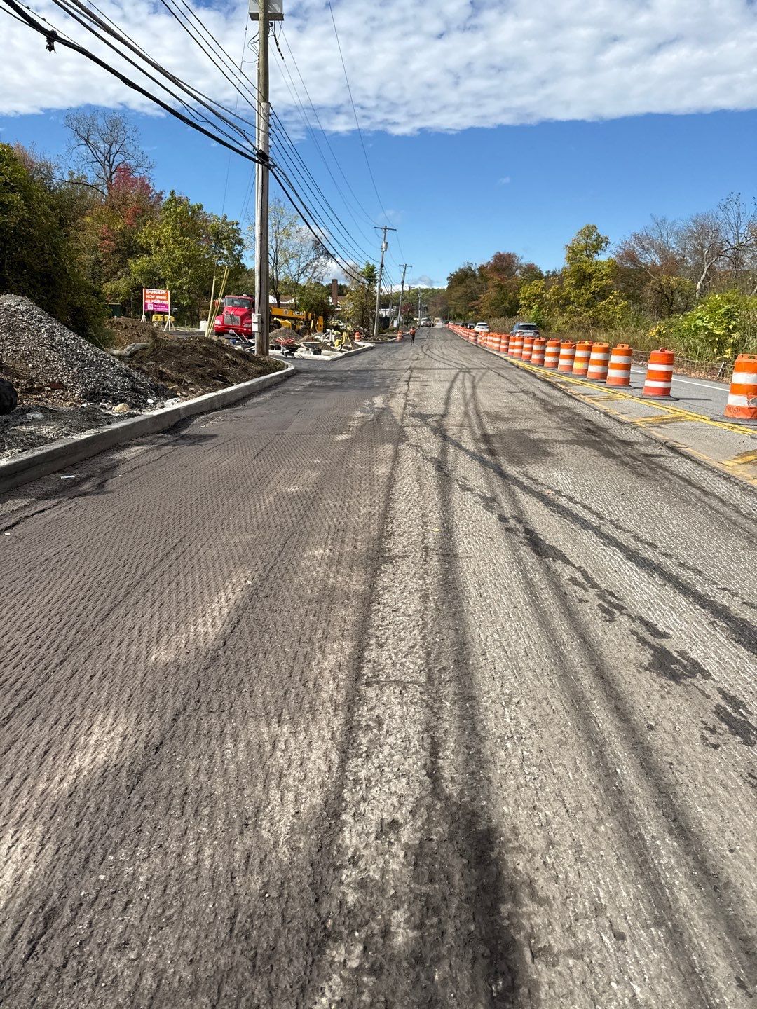 Road under construction, freshly milled surface. Orange traffic barrels line the right side.