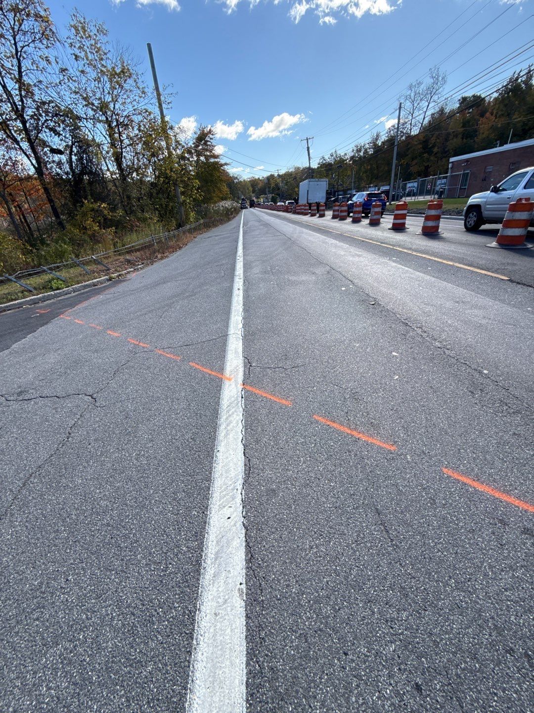 Road with a white center line, construction cones, and cars on the right. Bright blue sky.