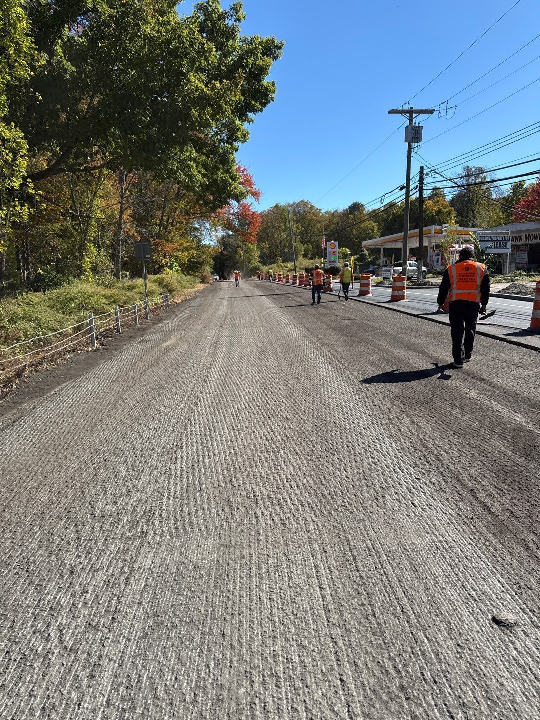 Road construction: Workers in safety vests on a textured road surface under a clear sky.
