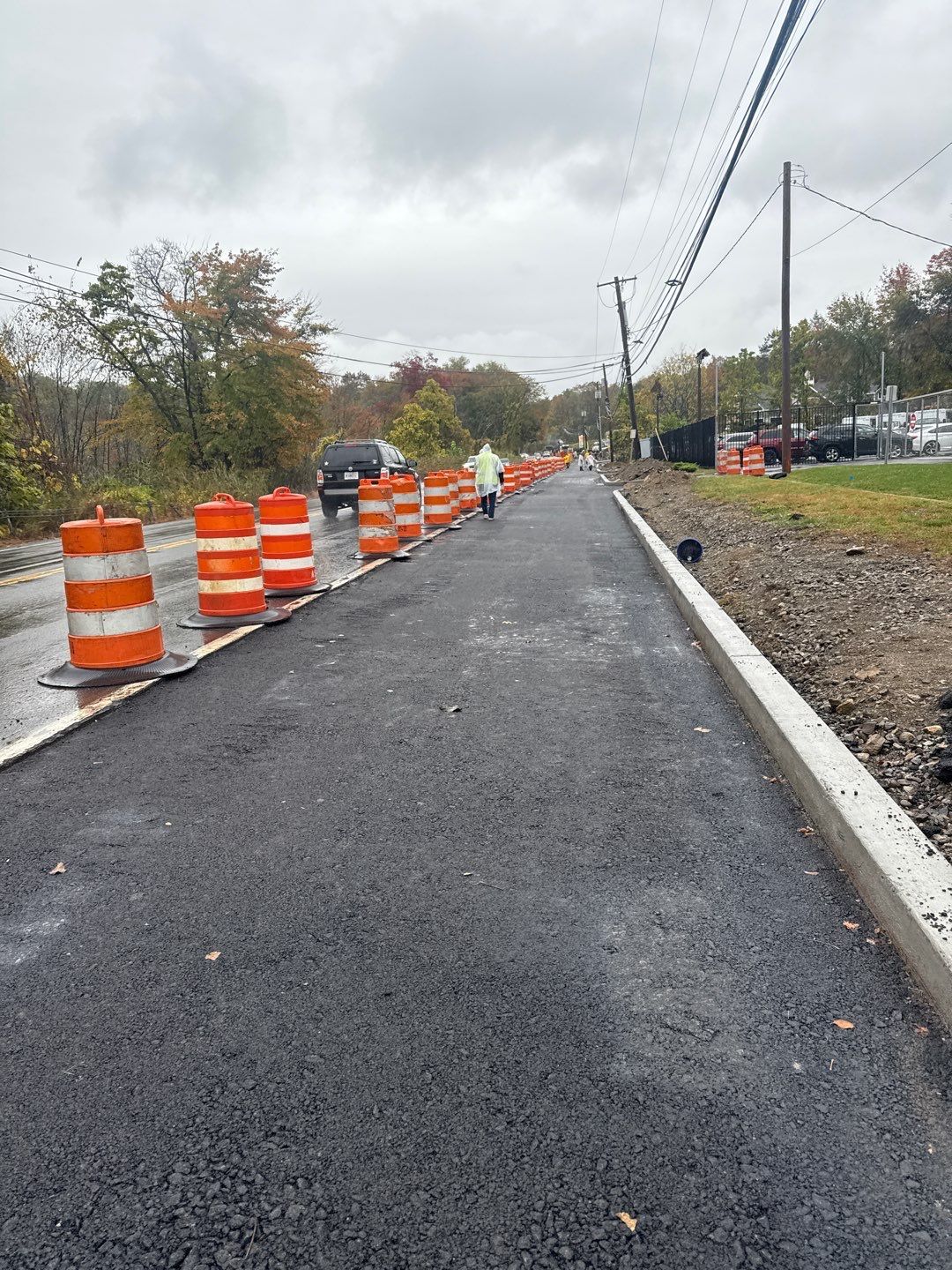 Newly paved road with orange safety barrels and a person in the distance, overcast day.
