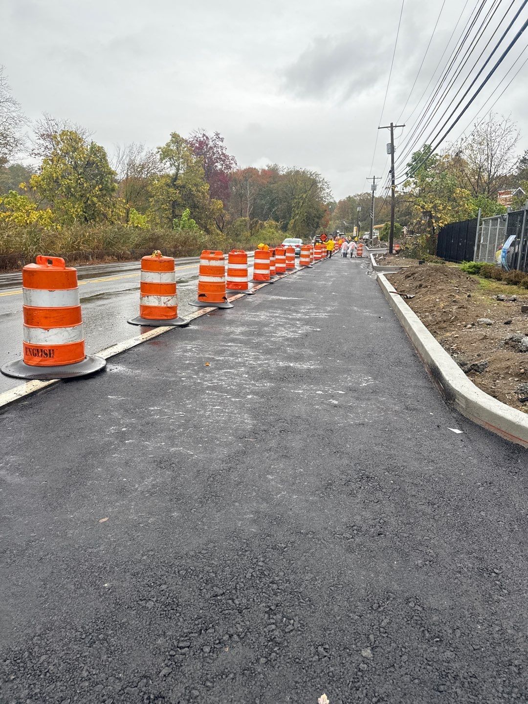 Road construction with orange traffic barrels lining a newly paved road.