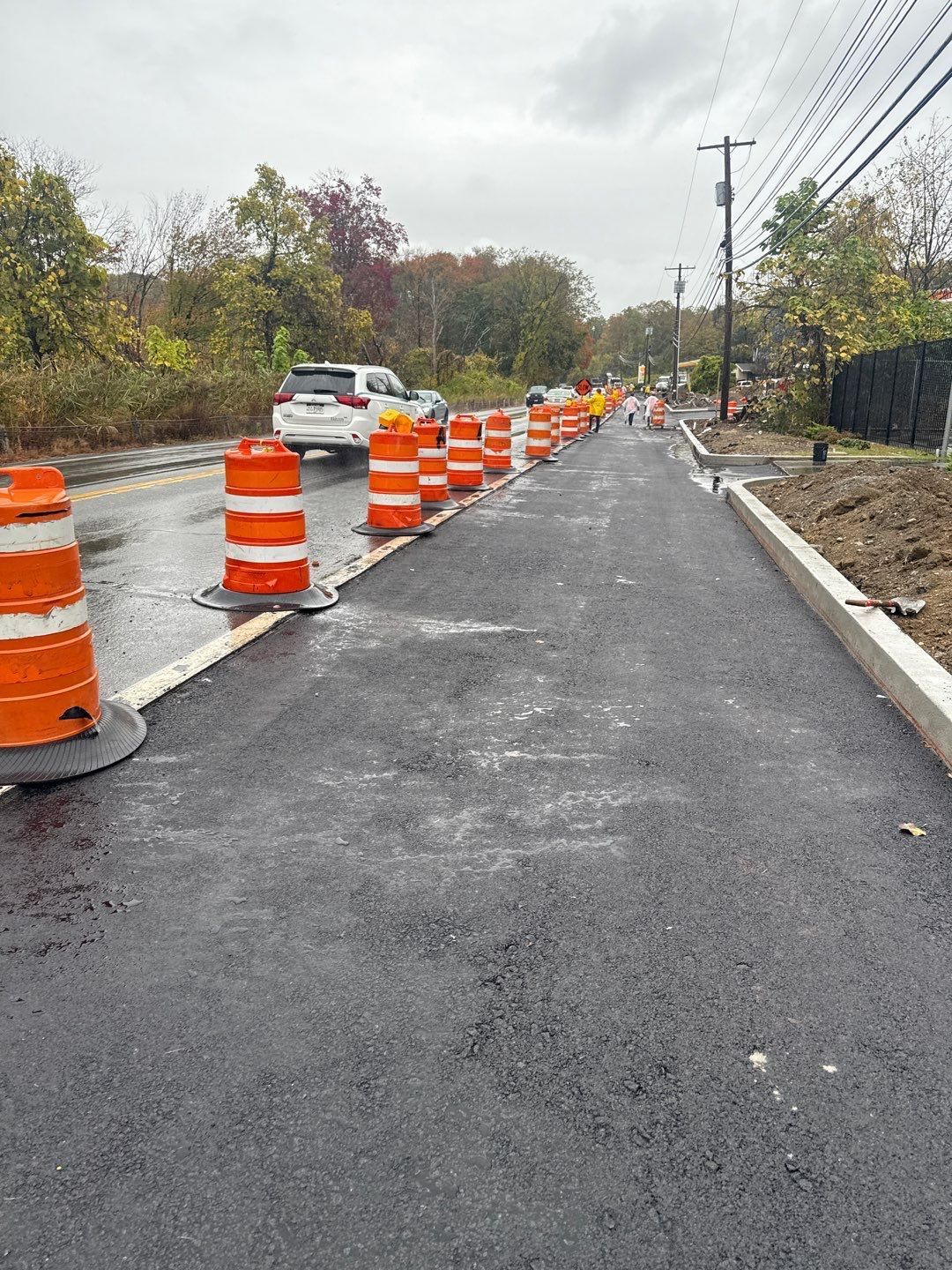 Road construction scene with orange cones, new asphalt, and a white car.