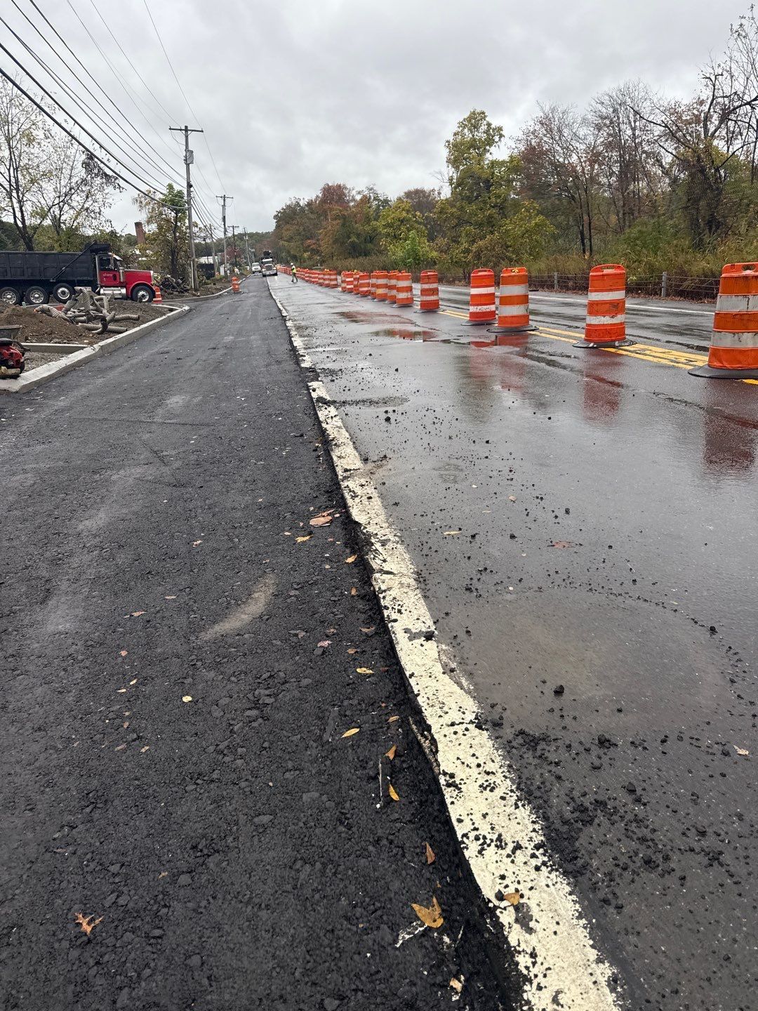 Road construction with orange cones and freshly paved asphalt on a cloudy day.