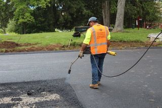 A man in an orange vest is spraying asphalt on a road.