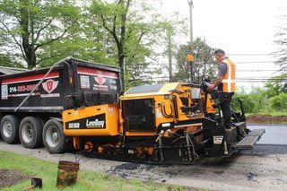 A man is standing next to a machine that is laying asphalt on a road.