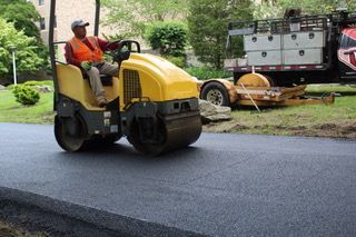 A man is driving a yellow roller on a road.