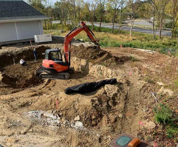 An excavator is digging a hole in the dirt in front of a house.