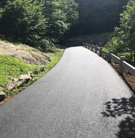 A road with a fence on the side of it going through a forest.