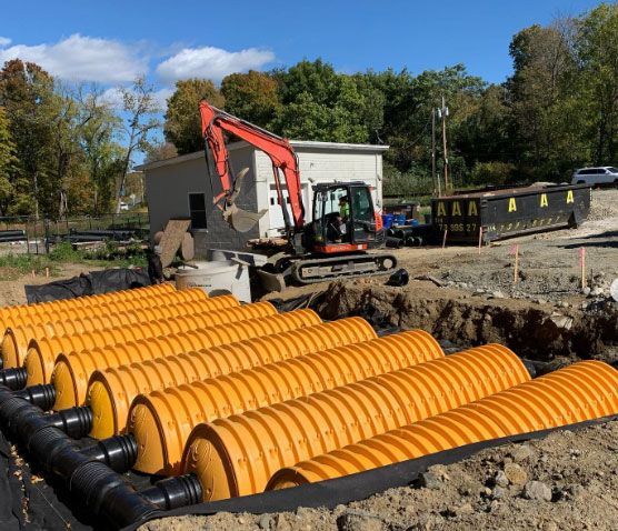 A row of orange pipes are sitting in the dirt next to a bulldozer.