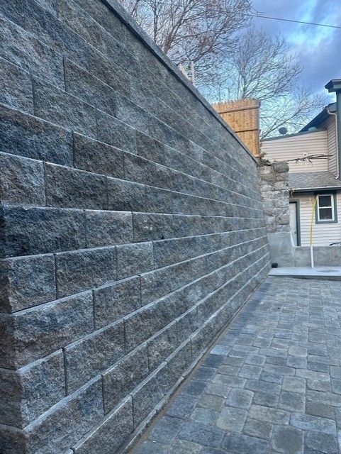 A large brick wall is surrounded by a brick walkway and a house.