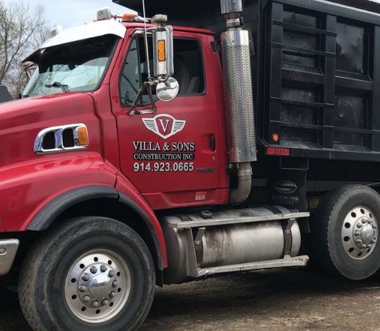 A red dump truck from villa & sons is parked in the dirt
