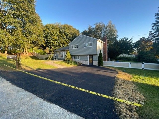 A house with a fence and a driveway is surrounded by yellow tape.