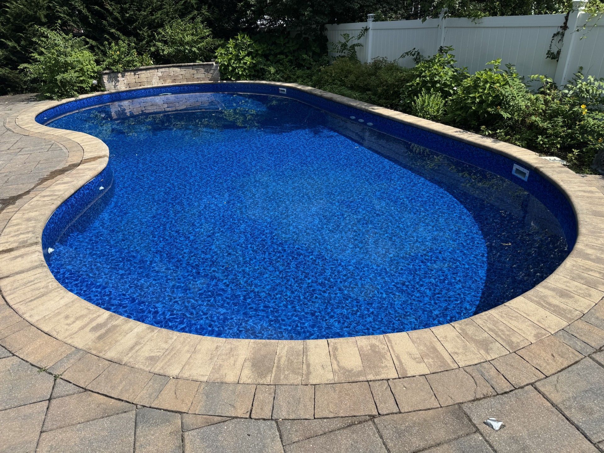 A blue, kidney-shaped swimming pool with brick coping surrounded by a stone patio.