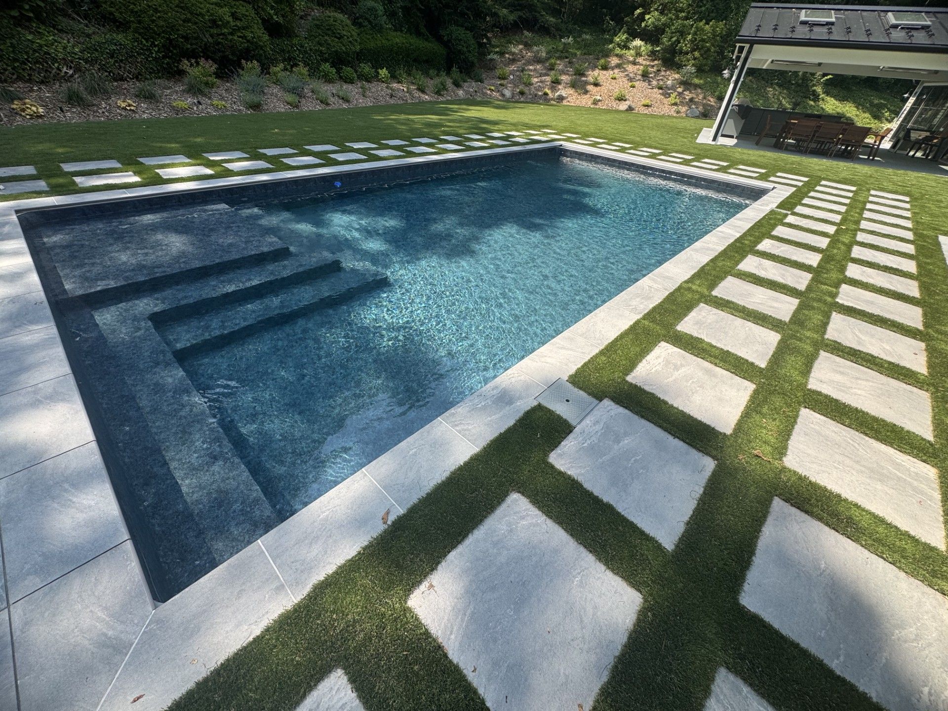 Rectangular pool with dark blue water and stone steps. Stone pathway and grass surround the pool.