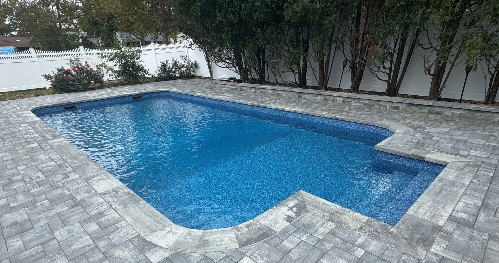 A large swimming pool is sitting on top of a brick patio.