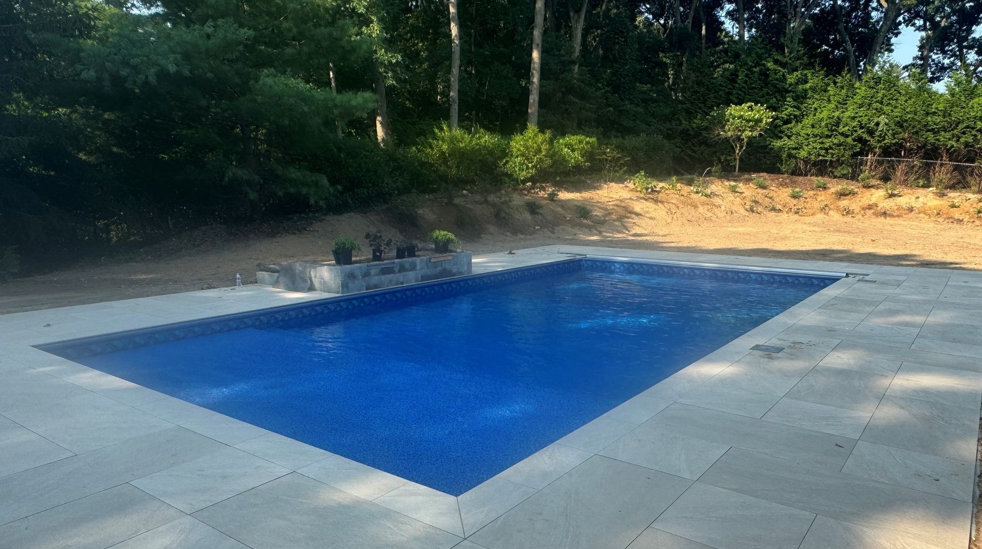 A large blue swimming pool is surrounded by trees and a patio.