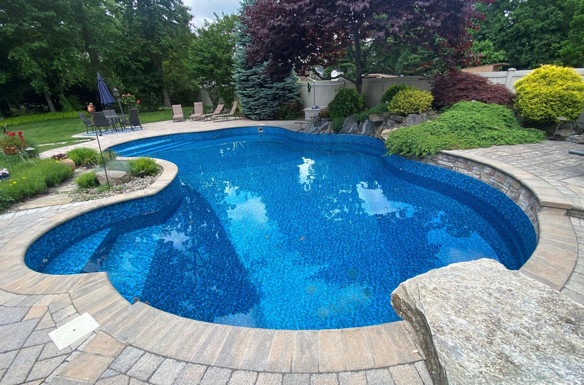 A large blue swimming pool surrounded by bricks and trees