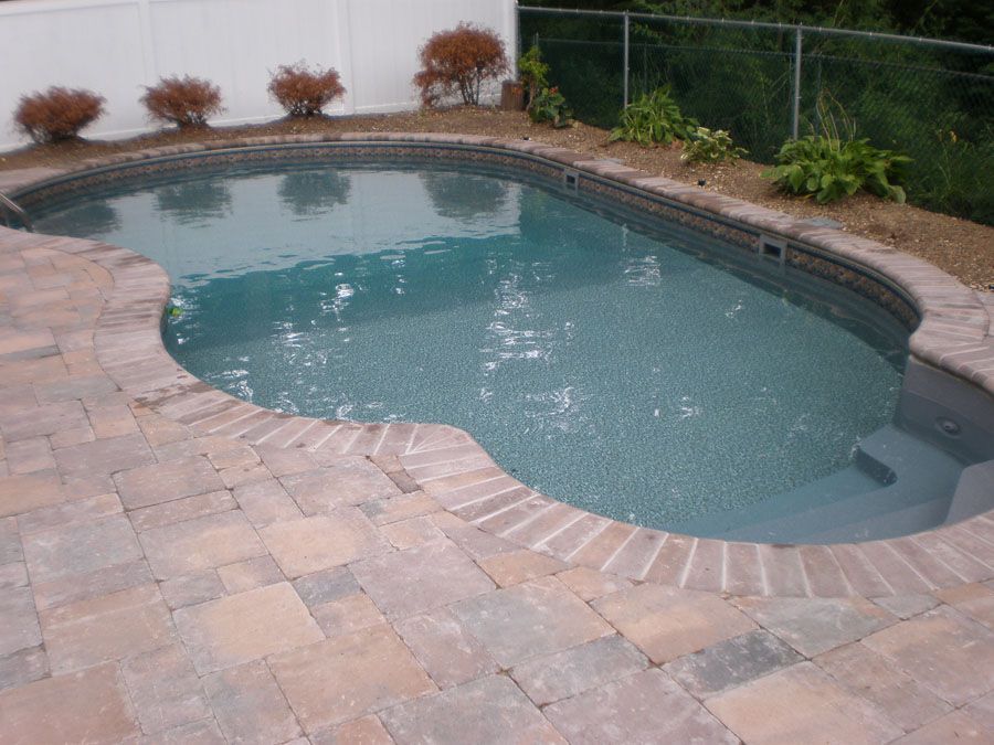 A large swimming pool surrounded by bricks and a fence