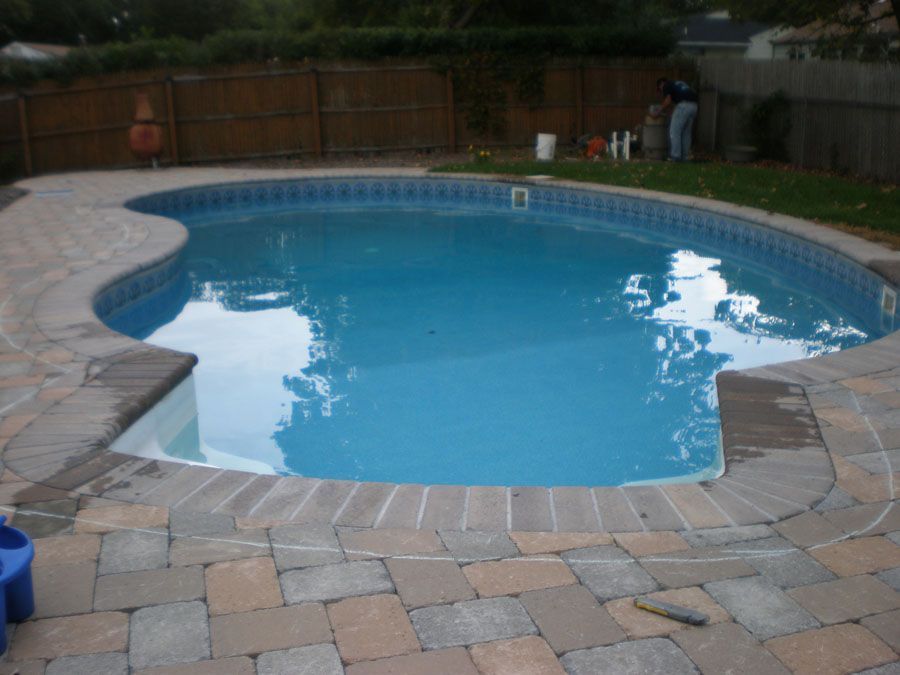 A large swimming pool is surrounded by bricks and a fence