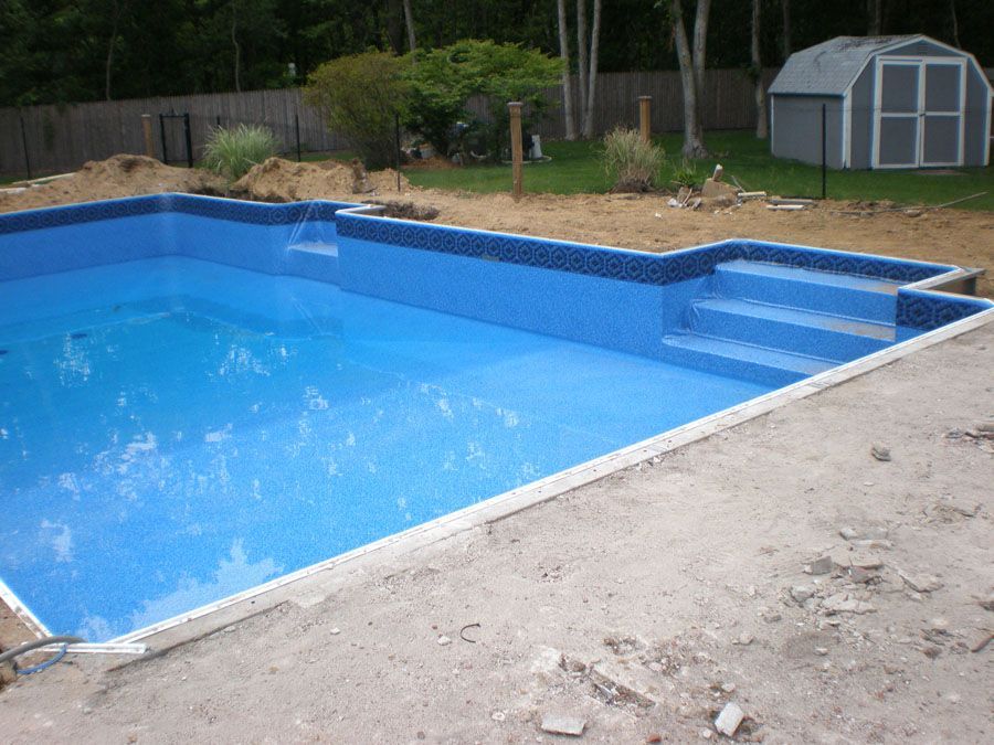 A large blue swimming pool with stairs and a shed in the background