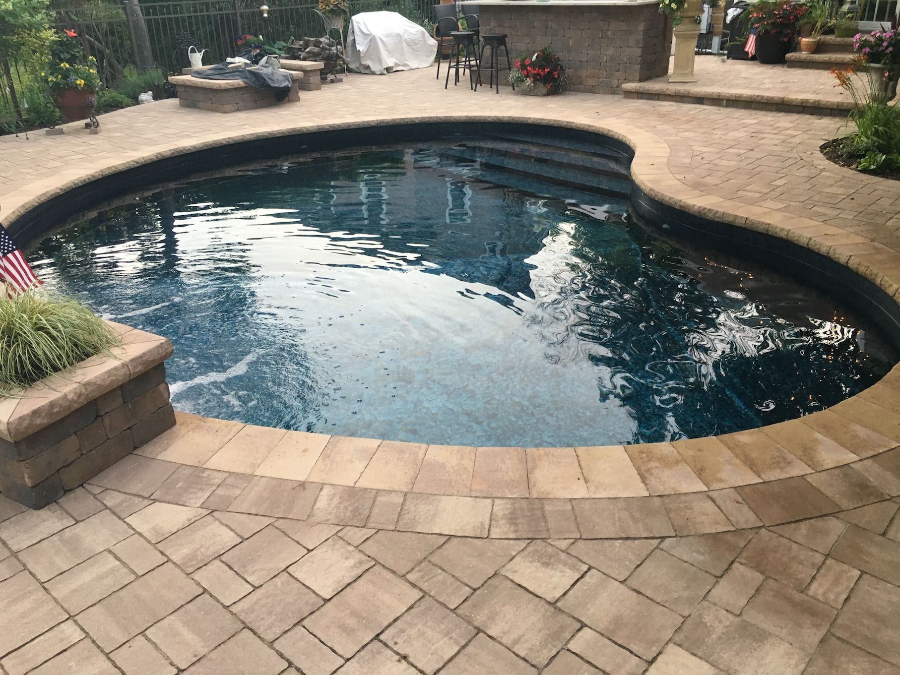 A large swimming pool is surrounded by a brick patio.