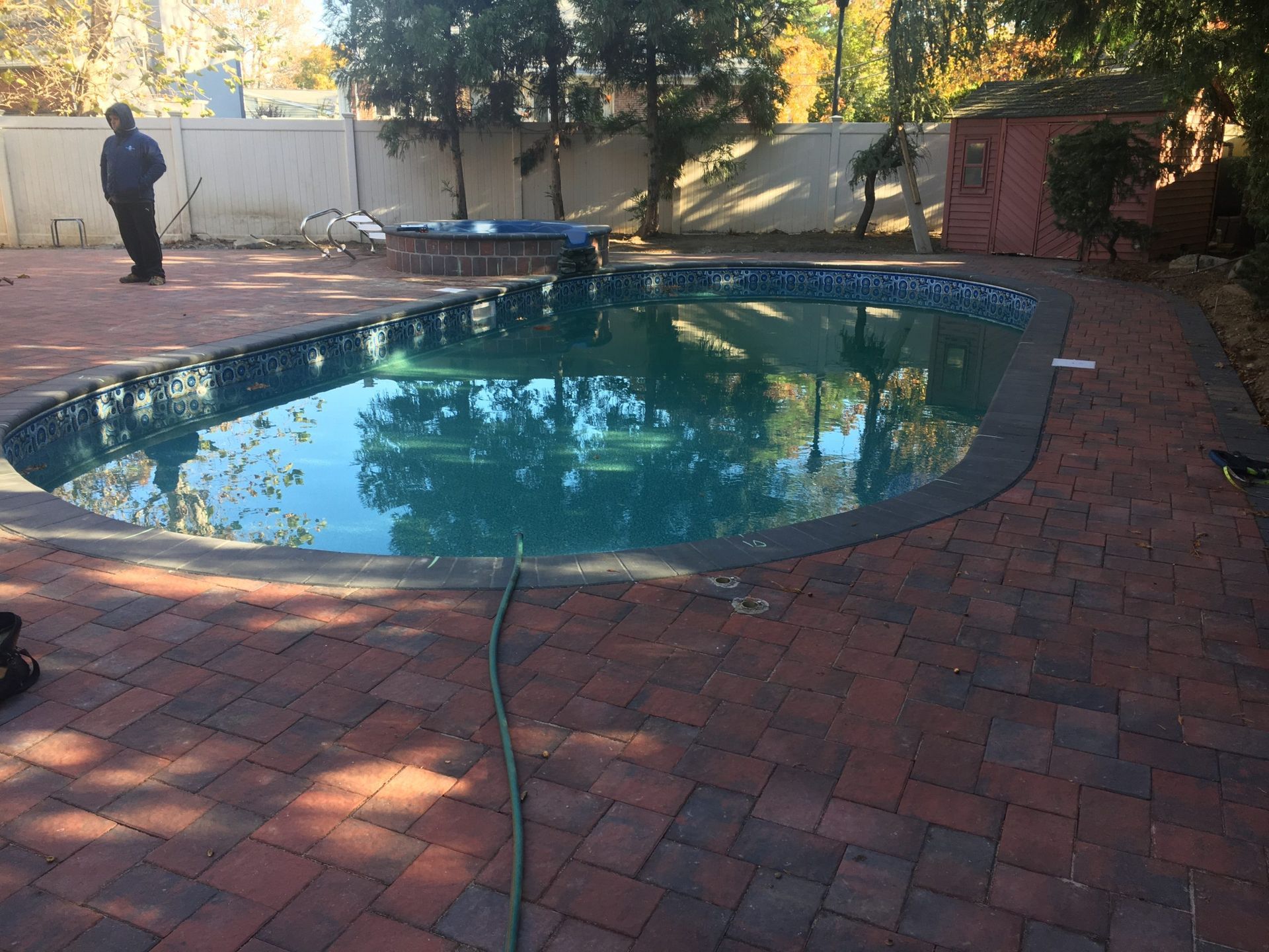 A man is standing next to a swimming pool on a brick patio.