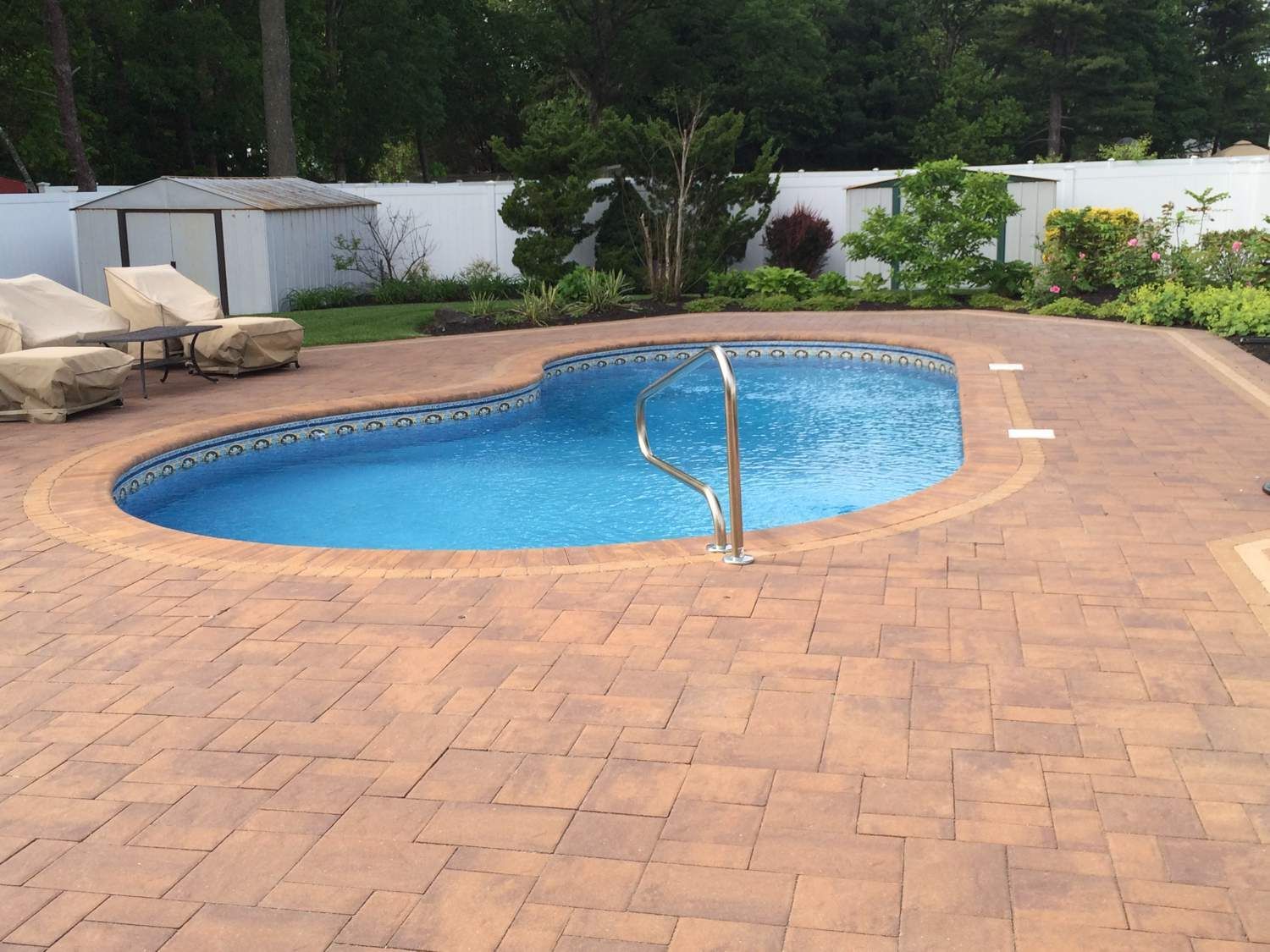 A large swimming pool is surrounded by a brick patio