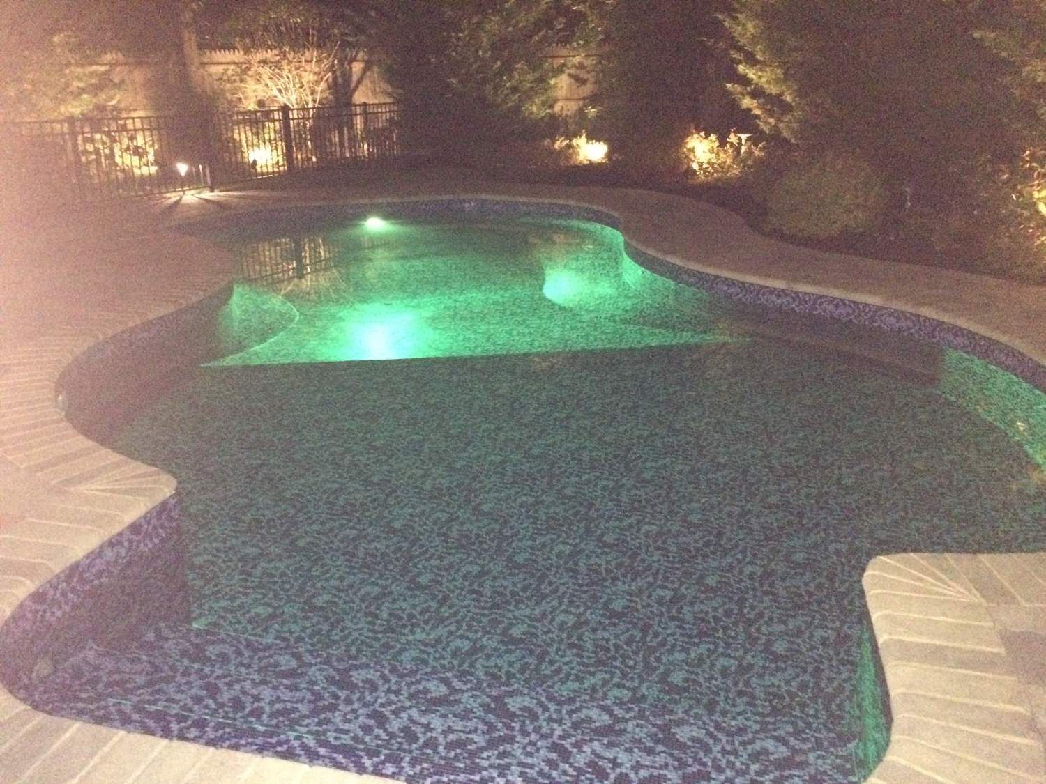 A large swimming pool is lit up at night with green lights