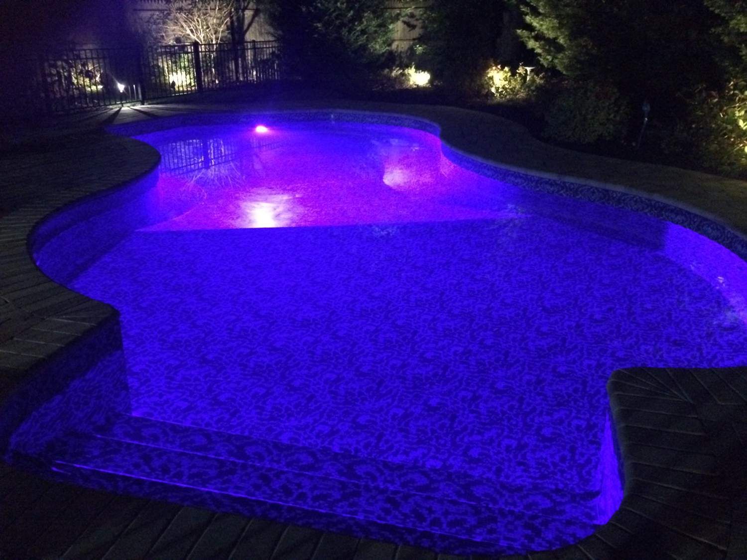 A swimming pool is lit up with purple lights at night.