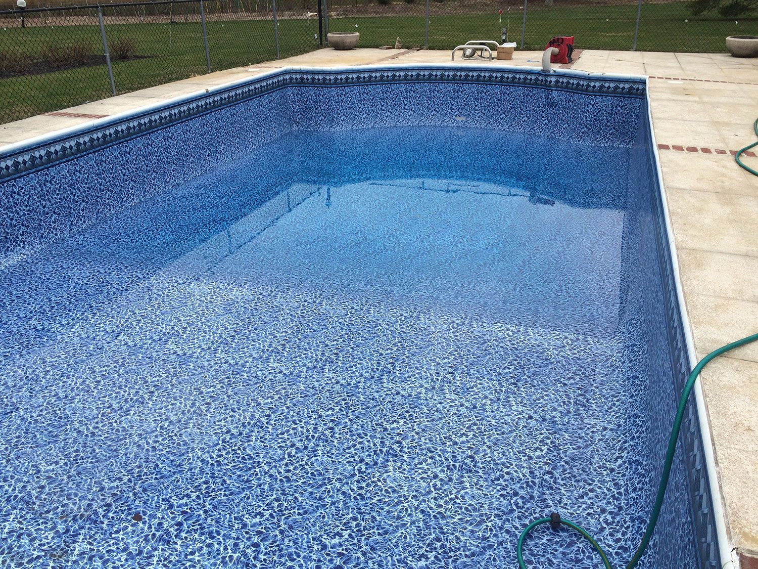 A large swimming pool with a green hose attached to it.