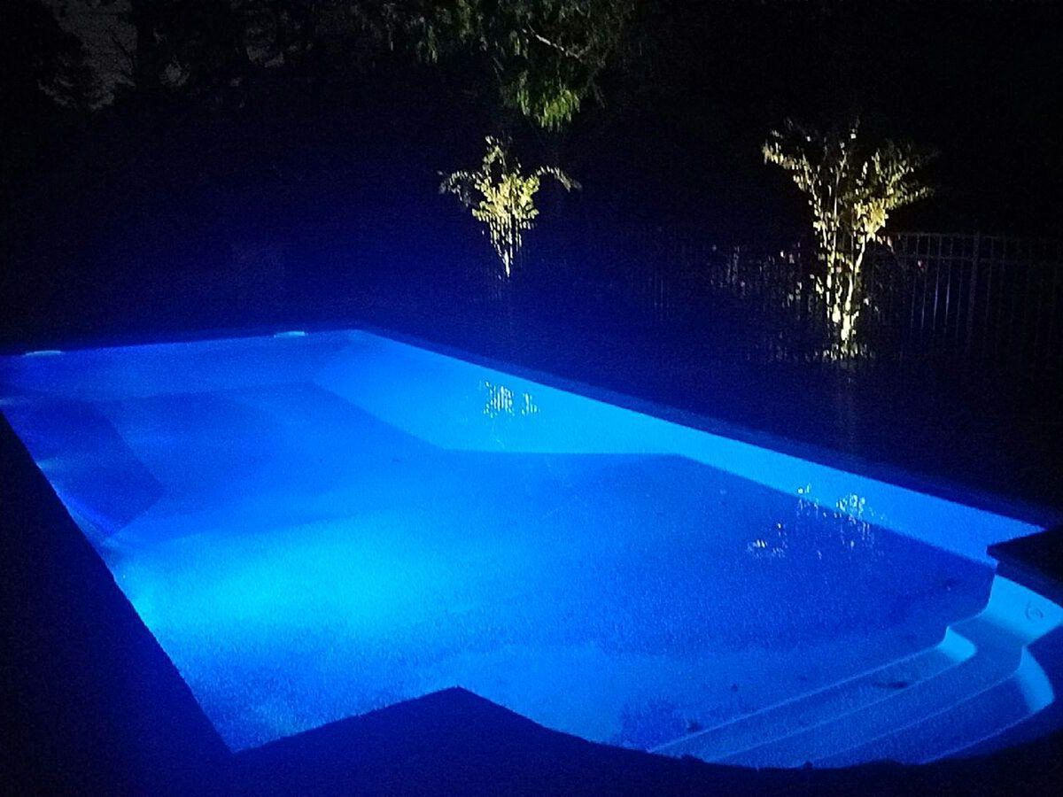 A swimming pool is lit up at night with blue lights