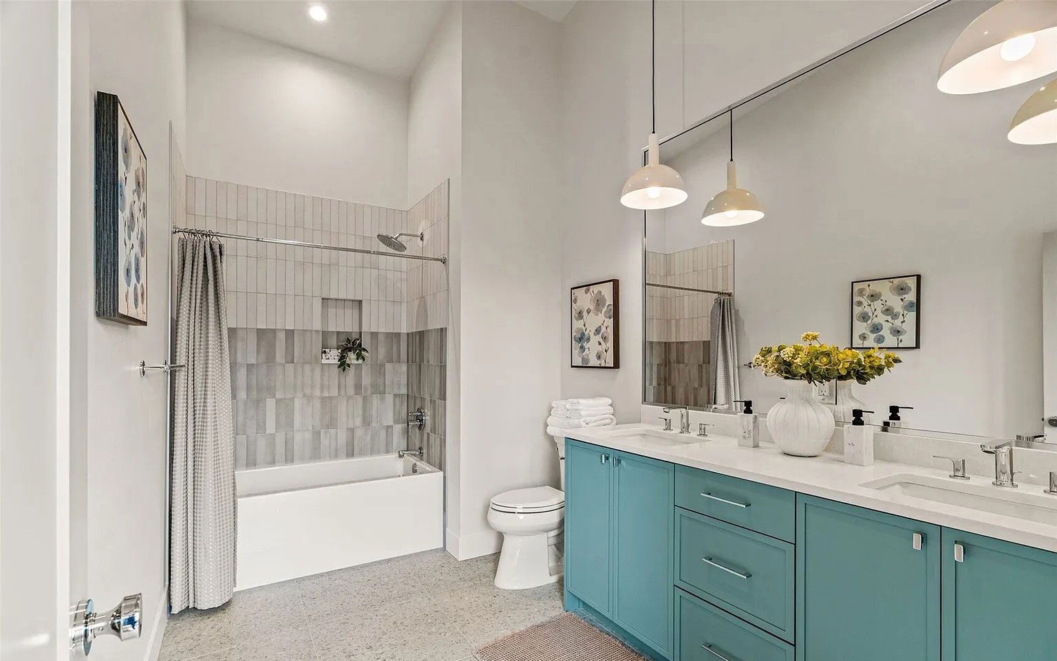 Bright bathroom with blue vanity, double sinks, mirror, and a white tiled bathtub/shower area