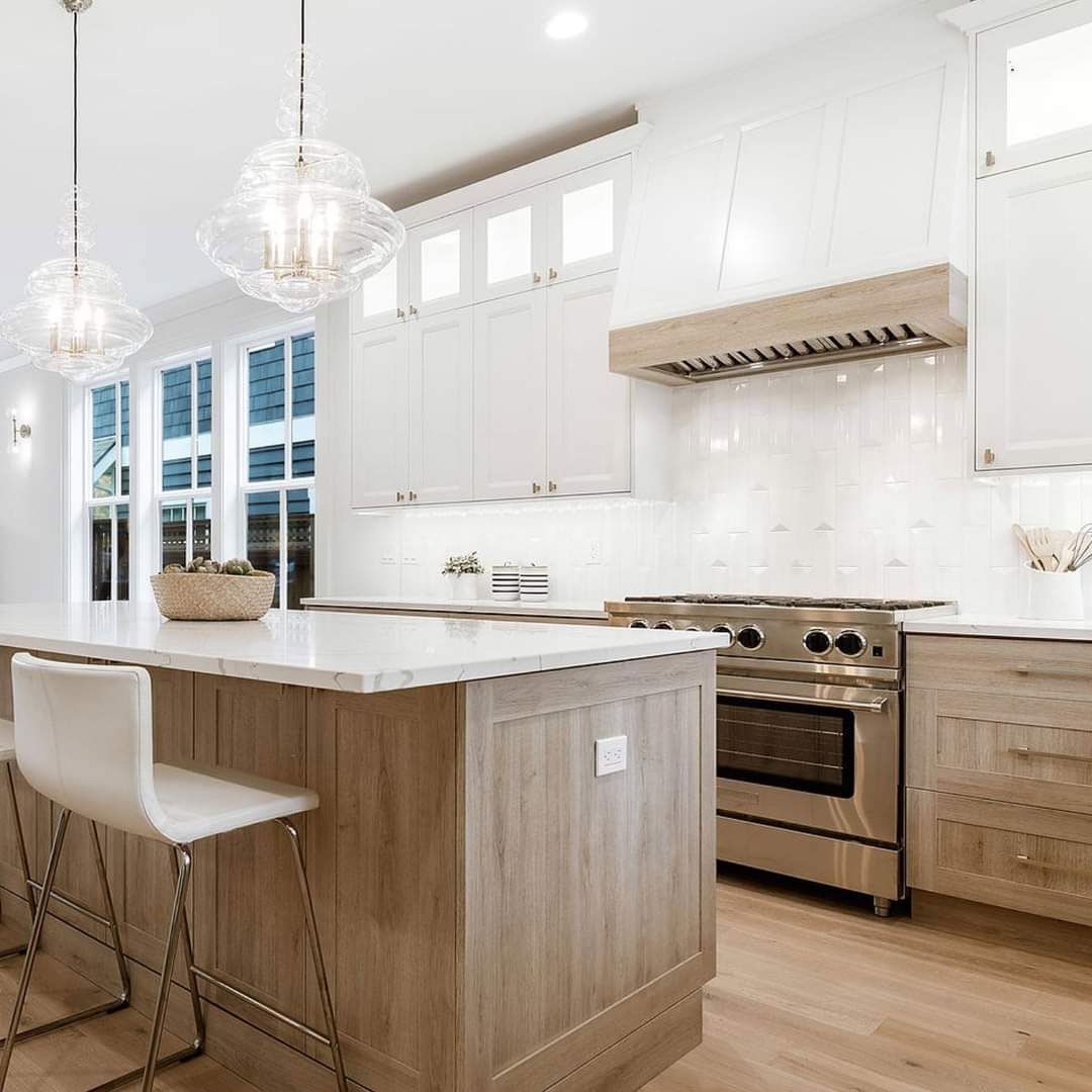 Bright white kitchen with wood island, bar stools, stainless range, and marble countertops